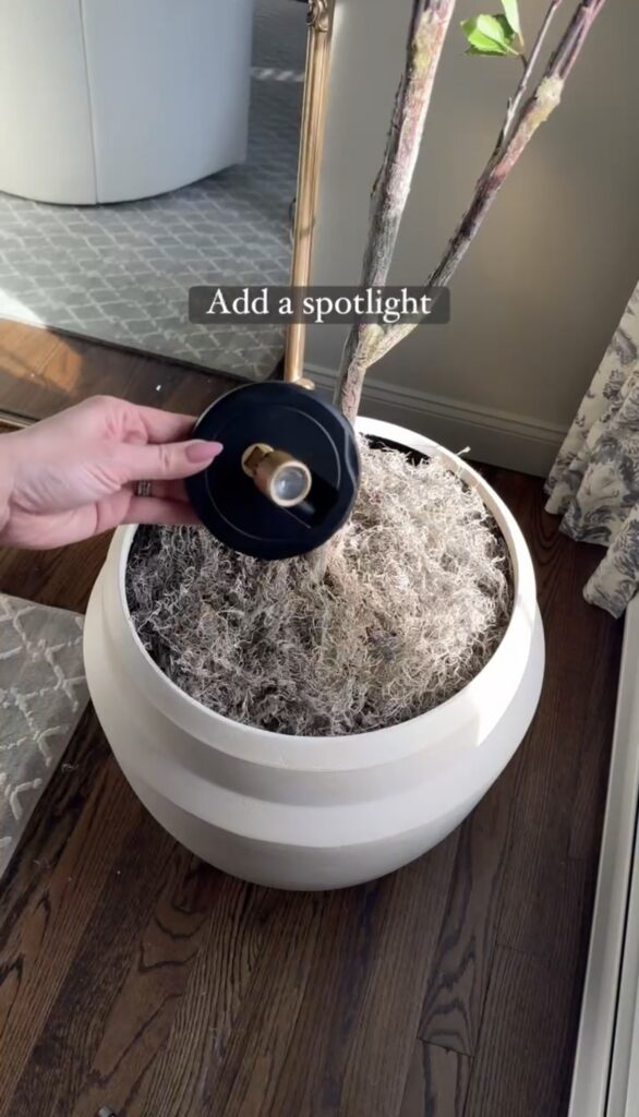 Wireless LED spotlight sitting on top of spanish moss inside planter with faux tree.