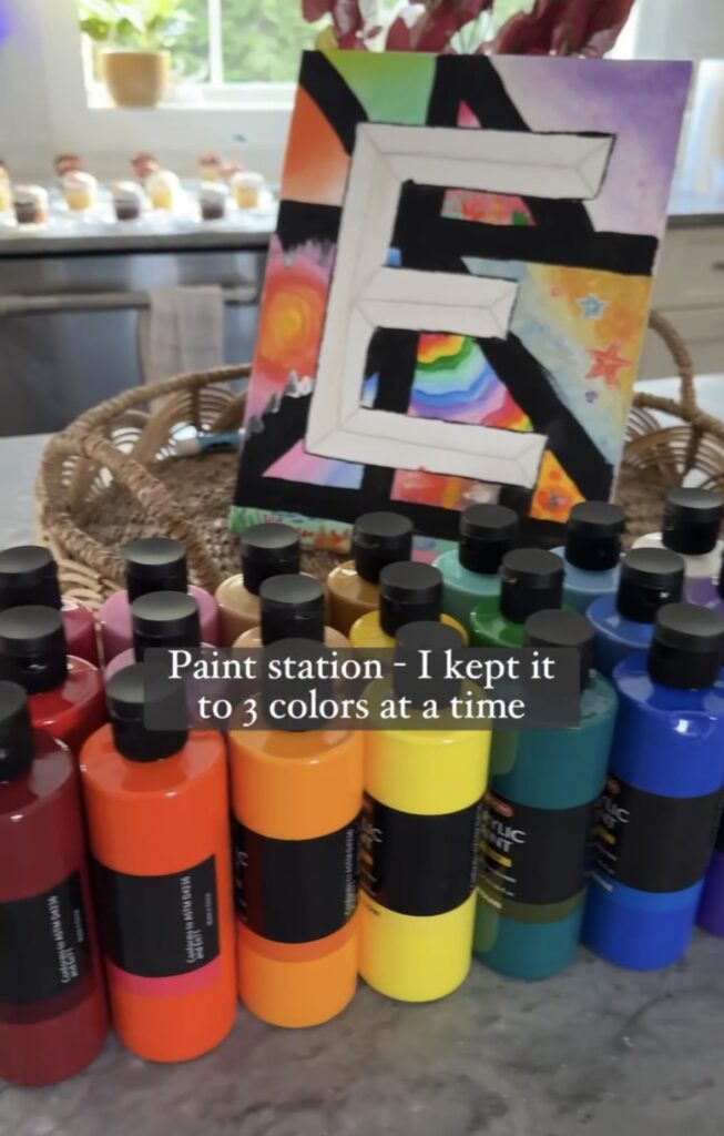 Display of various acrylic paint bottle colors arranged on a counter with painted canvas in basket.