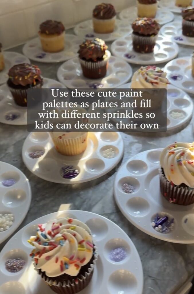 Frosted cupcakes sitting on top of paint palettes with sprinkle decorations on top. 