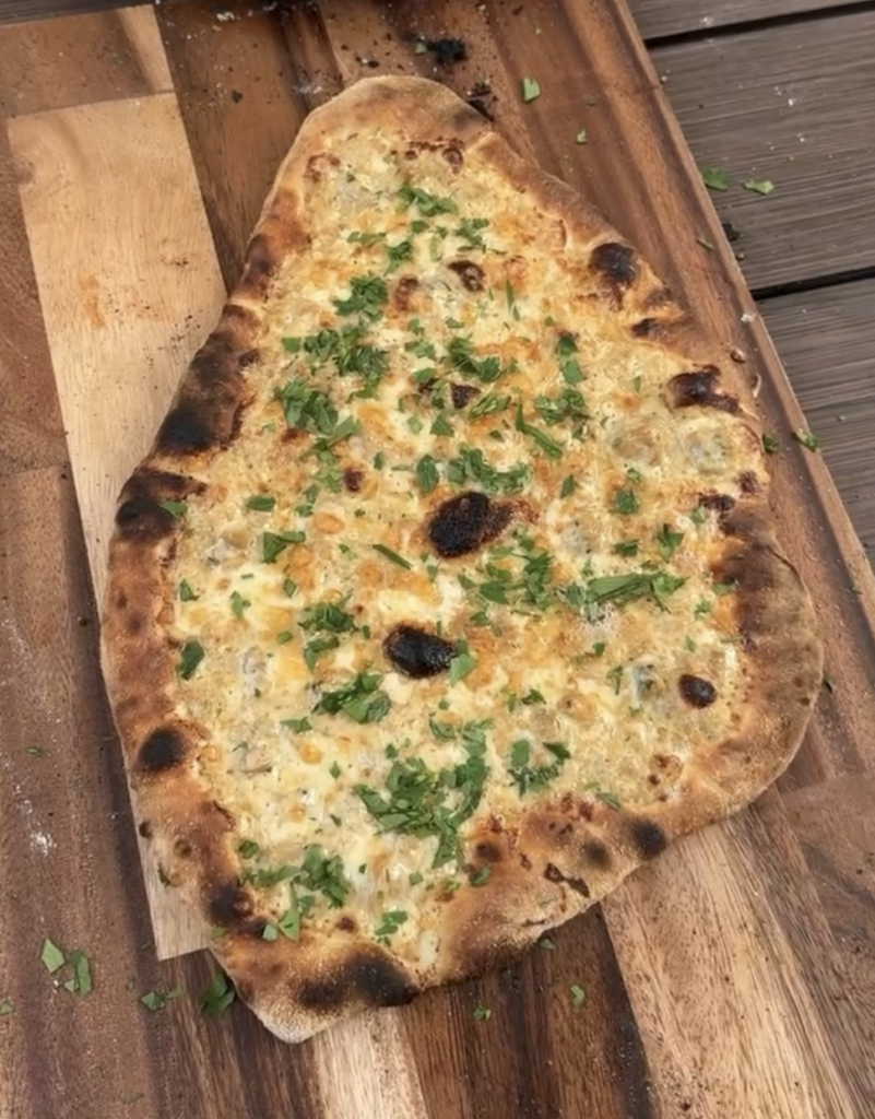 White clam pizza cooling on a wooden board.