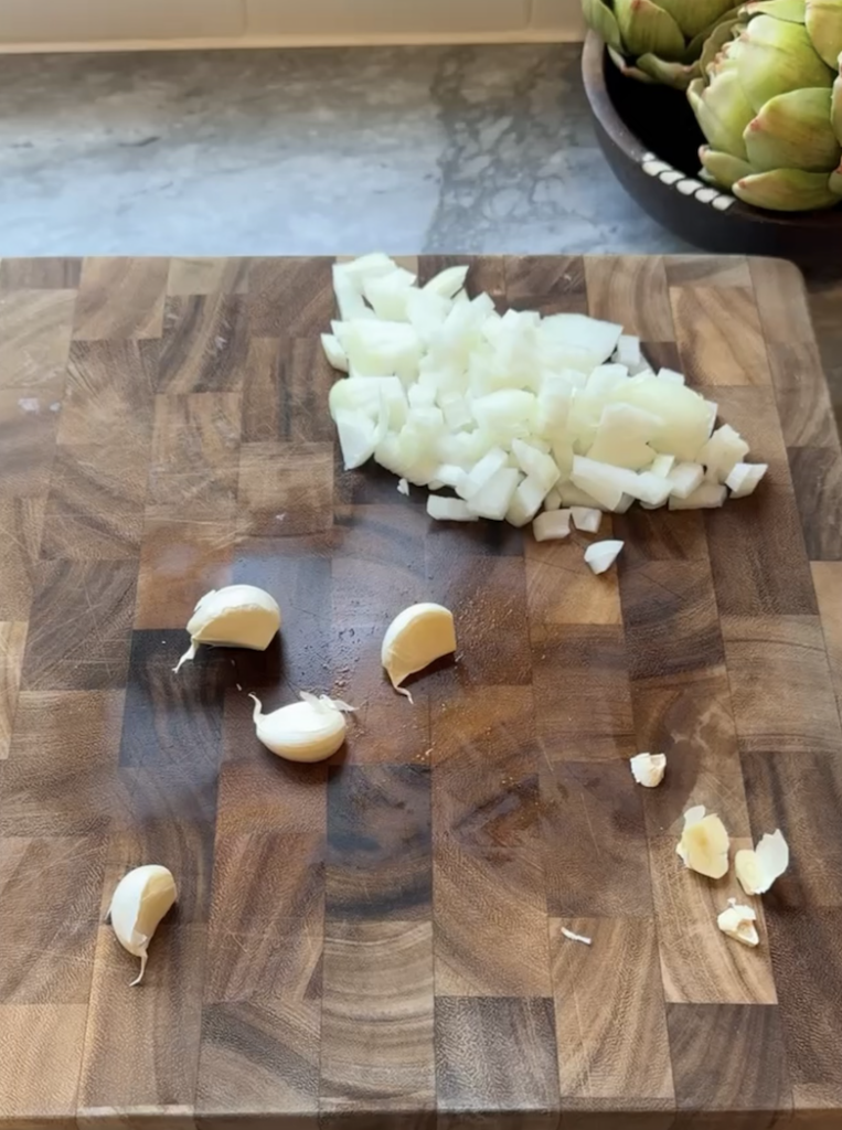 Ingredient prep showing pile of diced onion and garlic cloves on wooden board. 