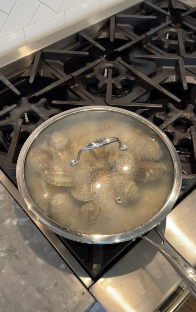 Closed lid covering clams cooking in white wine.