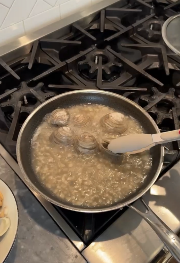 Opened clams being taken out of saucepan with tongs.