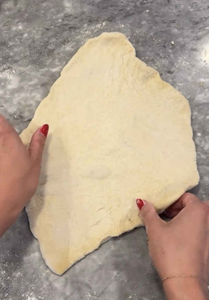 Stretched out pizza dough spread on floured surface. 