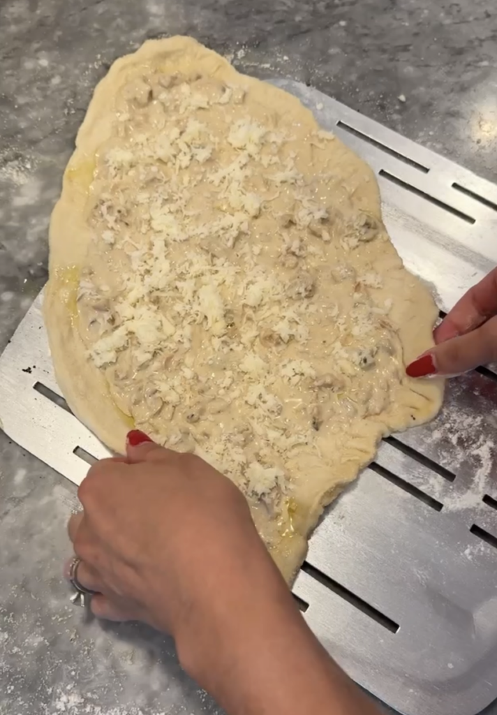 White clam pizza being guided onto floured pizza peel.