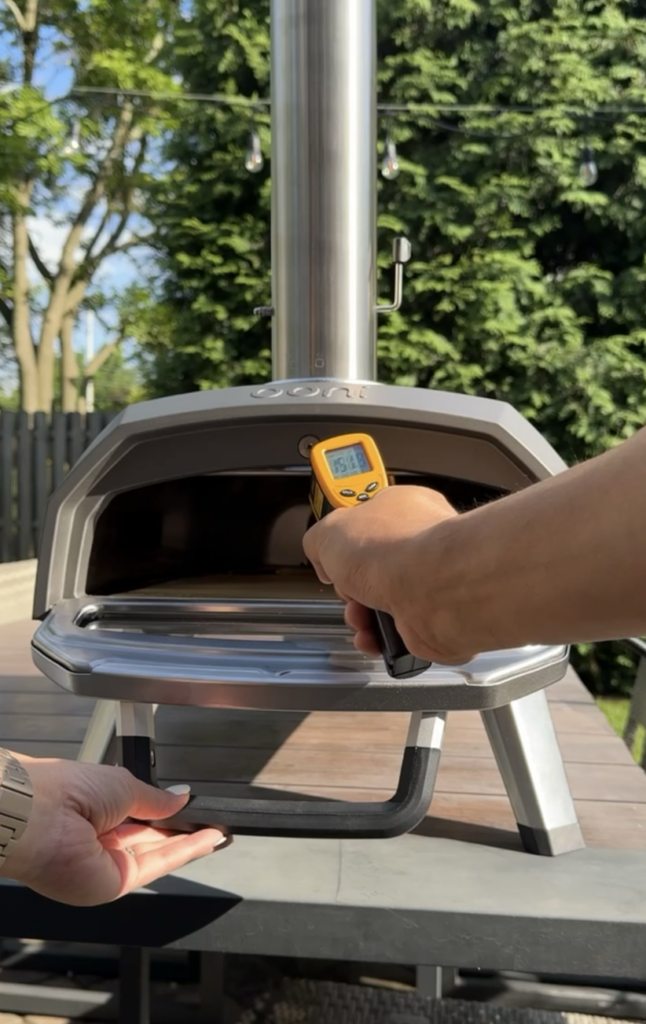 Ooni pizza oven setup outside with infrared thermometer reading temperature.