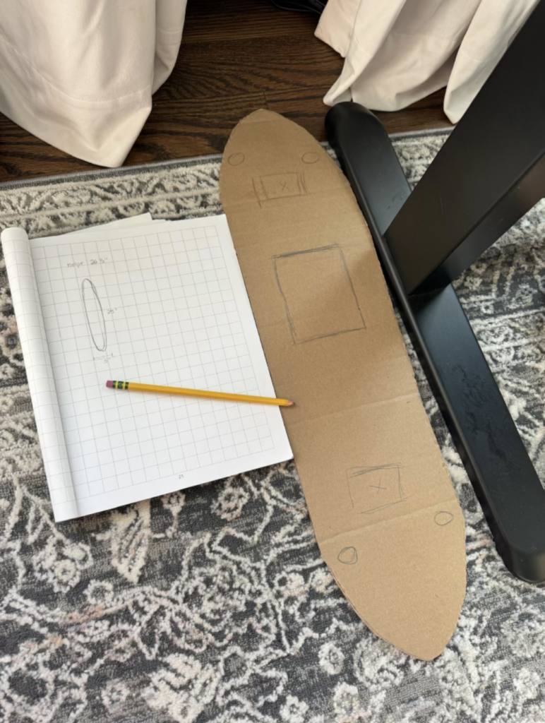 Cardboard cutout of oval shape with measurements to desk legs.